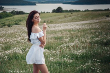 Beyaz elbiseli güzel esmer kadın papatya tarlasında baharın tadını çıkarıyor. Sağlık fikri ve konsept, güzel sağlıklı saç ve deri, alerji eksikliği.