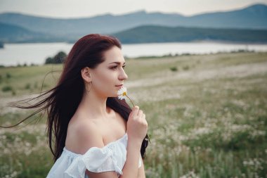 Beyaz elbiseli güzel esmer kadın papatya tarlasında baharın tadını çıkarıyor. Sağlık fikri ve konsept, güzel sağlıklı saç ve deri, alerji eksikliği.