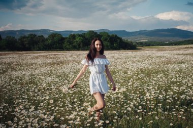 Beyaz elbiseli güzel esmer kadın papatya tarlasında baharın tadını çıkarıyor. Sağlık fikri ve konsept, güzel sağlıklı saç ve deri, alerji eksikliği.