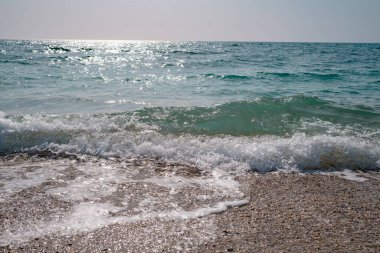 İlkbaharda öğle vakti güzel deniz, berrak su, kayalık sahil. Sessiz dalgalar gün ortası güneşiyle aydınlanır.