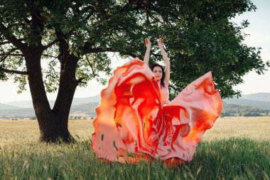 Yeşil yaz arka planında güzel aktif özgür kız. Bir tarlada dans eden güzel pembe bir elbiseyle güçlü bir meşe ağacının yanında