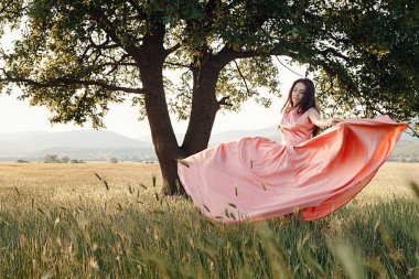 Yeşil yaz arka planında güzel aktif özgür kız. Bir tarlada dans eden güzel pembe bir elbiseyle güçlü bir meşe ağacının yanında