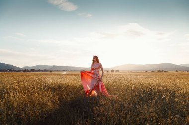 Gün batımında güzel pembe bir elbiseyle tarlada dans eden bir kız. Reklam için ideal ve fotoğraf güneşi parlak ve sulu.