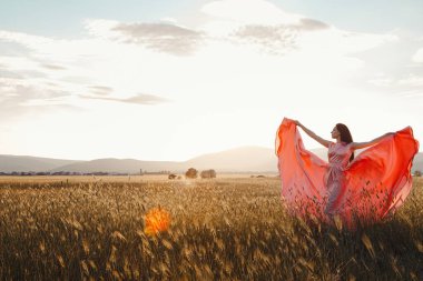 Gün batımında güzel pembe bir elbiseyle tarlada dans eden bir kız. Reklam için ideal ve fotoğraf güneşi parlak ve sulu.