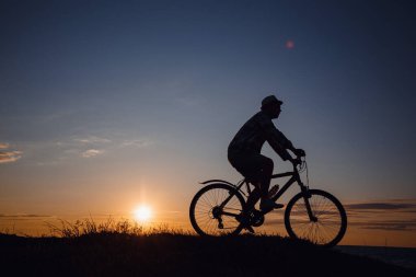 Günbatımı arka planında bisiklete binen hippi bir adamın silueti. Fikir ve konsept fiziksel aktivite ve sağlıklı yaşam tarzı