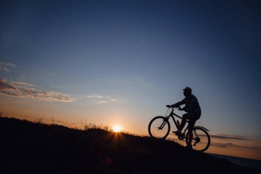 Günbatımı arka planında bisiklete binen hippi bir adamın silueti. Fikir ve konsept fiziksel aktivite ve sağlıklı yaşam tarzı