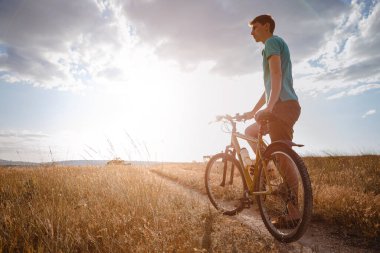 Günbatımında bisikletle gezen yakışıklı bir adam, sağlıklı, aktif bir hayat tarzı gezgini. Kırsalda gün batımında toprak yolda