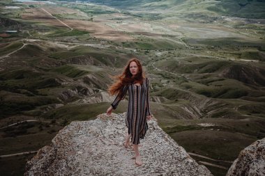 Kızıl saçlı özgür kadın seyahatin tadını çıkarıyor. Klimentieva Dağı, Kırım 'da bir uçurumun kenarında giyinmiş bir kadın manzaraya bakıyor.