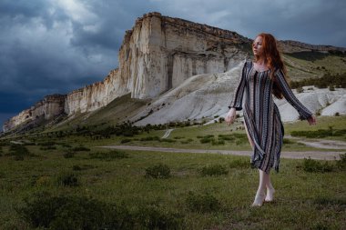 Tarladaki dramatik fırtına manzarası üzerinde soluk soluğa duran genç, moda kızıl kadın. Kırım, Beyaz Kaya Belogorsk yakınlarında.