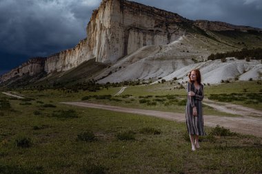Tarladaki dramatik fırtına manzarası üzerinde soluk soluğa duran genç, moda kızıl kadın. Kırım, Beyaz Kaya Belogorsk yakınlarında.