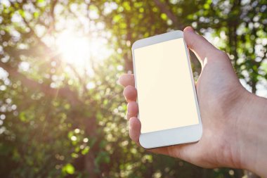 Erkek eli beyaz akıllı telefon, cep telefonu, yeşil orman arka planının bulanık görüntüsü üzerinde cep telefonu..