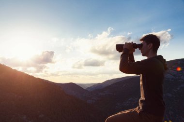 Dağın tepesindeki genç adam dürbünle kanyon manzarasına bakıyor. Fotokopi alanı olan pankart. Fikir ve seyahat kavramı ve keşifler, maceralar ve özgürlük