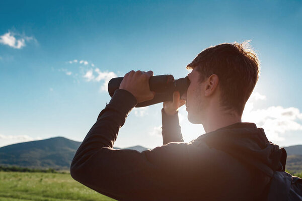 Young man at mountain looking through binoculars. Banner with copy space. idea and concept of travel and discoveries, adventures and freedom