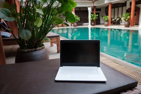 ホテルの美しいプールを背景にリモートデジタルノマドのラップトップ リモートワーク フリーランス テクノロジー インターネット 休暇の概念 — ストック写真