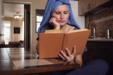 Havlu banyosundan sonra genç Asyalı kadın mutfakta kitap okuyor. Doğal güzellik sağlıklı model kendini izolasyondan zevk alıyor. Coronavirus önleme amaçlı sosyal medya kampanyası için evinizde kalın