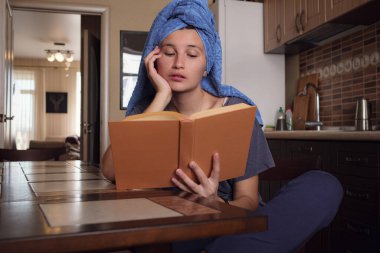 Havlu banyosundan sonra genç Asyalı kadın mutfakta kitap okuyor. Doğal güzellik sağlıklı model kendini izolasyondan zevk alıyor. Coronavirus önleme amaçlı sosyal medya kampanyası için evinizde kalın