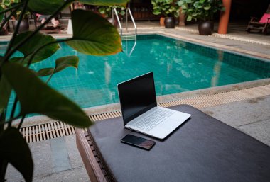 Havuzda beyaz dizüstü bilgisayar, akıllı telefon, tatilde serbest çalışan biri..