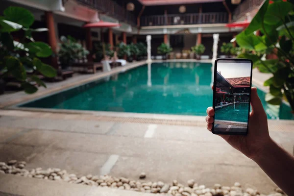 ホテルのプールを背景に携帯電話を持ってる 画面上の写真カメラ 手を上げてスマホで夏休みの写真を撮って — ストック写真