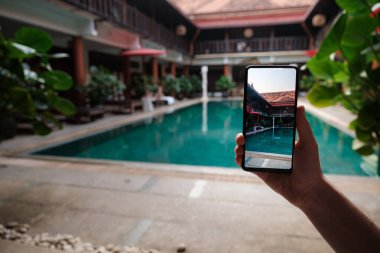 Oteldeki havuzun arka planında el ele tutuşan telefon. Ekrandaki fotoğraf makinesi. Kapat elini akıllı telefon yaz tatilinin fotoğrafını çek..