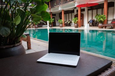 White laptop on the background of the pool in an exotic hotel. Conceptual workspace. Remote work, freelancer, internet, travel and vacation concepts. clipart