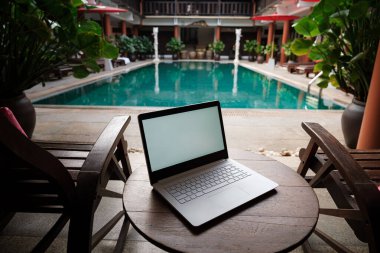 Ahşap masa yüzme arka planında beyaz bir dizüstü bilgisayar. Yeni bir günün başlangıcı. Serbest iş konsepti. Esnek uzaktan çalışma, seyahat, reklam ve kopyalama alanı