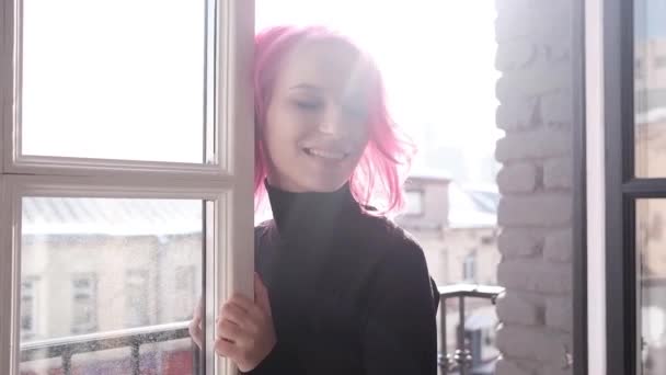 ピンク色の髪の美しい若い女性は彼女の部屋で晴れた朝を楽しんでいます 窓の暖かい日差し — ストック動画
