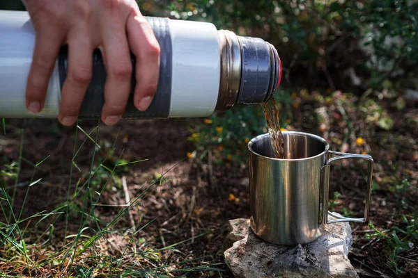 Kamp bardağında dişi bir el, doğadaki bir termostan çay doldurur. Mola, dinlenme ve seyahat fikri