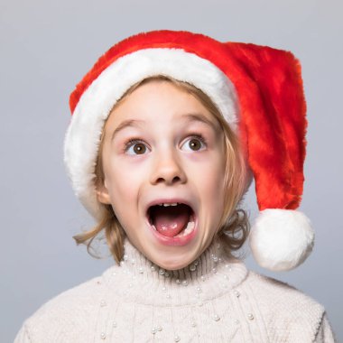 Şok olmuş ve şaşırmış kırmızı Noel şapkalı çocuk.