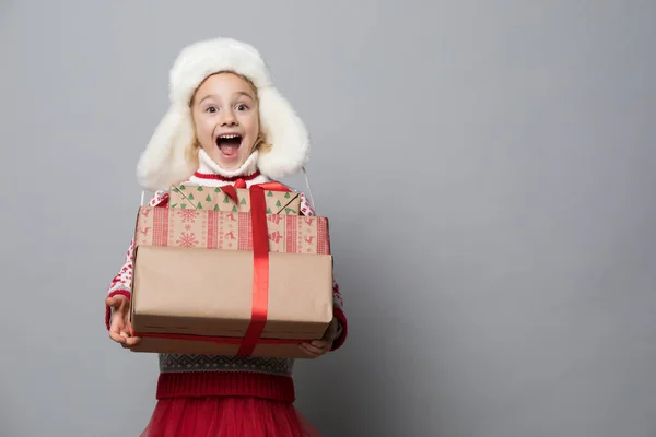 Smiling funny child in fluffy hat holding Christmas gift in hand. — Stock Photo, Image