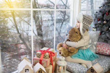 Pencerenin kenarında oturan küçük kız bir ayıyla