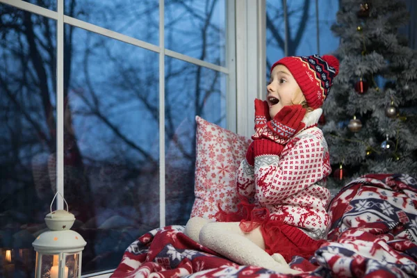 Niña sentada junto a la ventana y el árbol de navidad — Foto de Stock