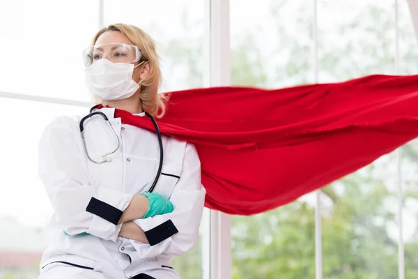 Доктор у супергеройському костюмі, що стоїть на захисті від пандемії вірусу на вікні — стокове фото
