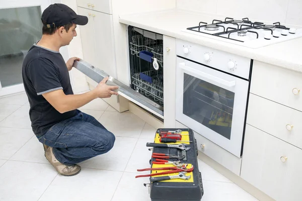 Man with tools repairing dishwasher in the kitchen