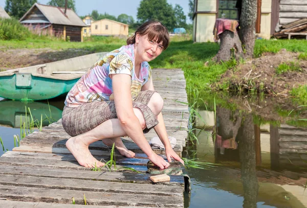 Ung kvinna tvättar kläder på träbryggan vid sjön på sommaren — Stockfoto