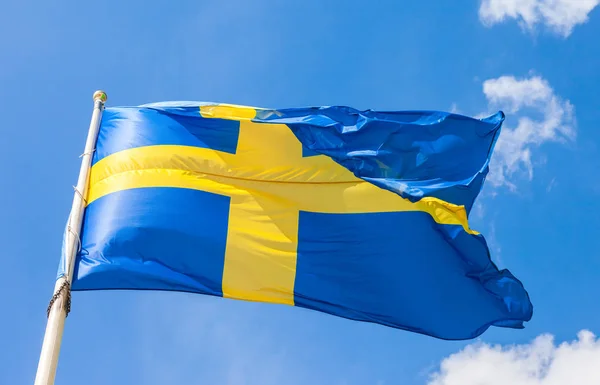Švédská vlajka s žlutý kříž, mával ve větru na modré obloze — Stock fotografie