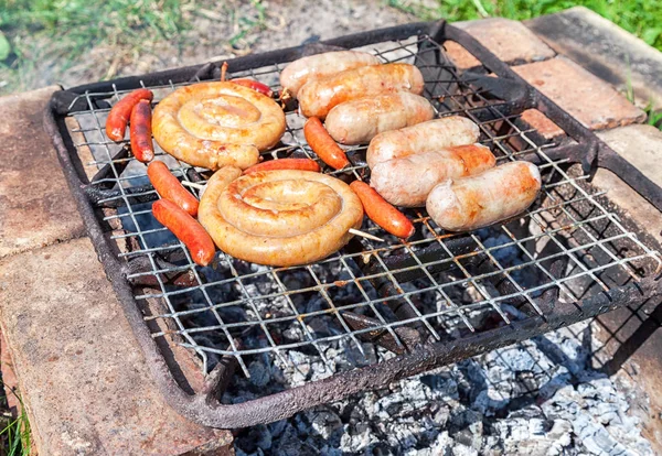 Delicious sausages on a metal grid grilling over hot coals for a
