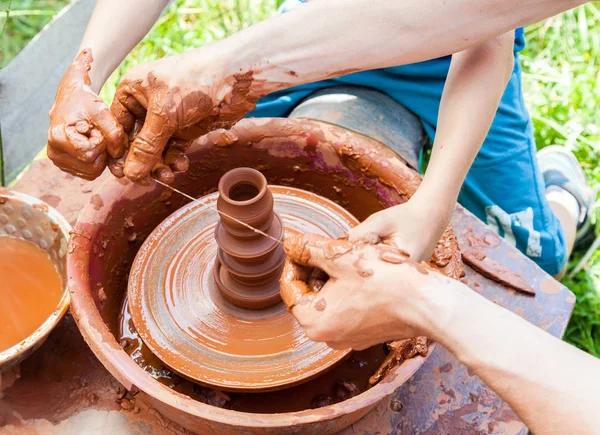 Teacher helps his student to work with red clay. Work on the pot