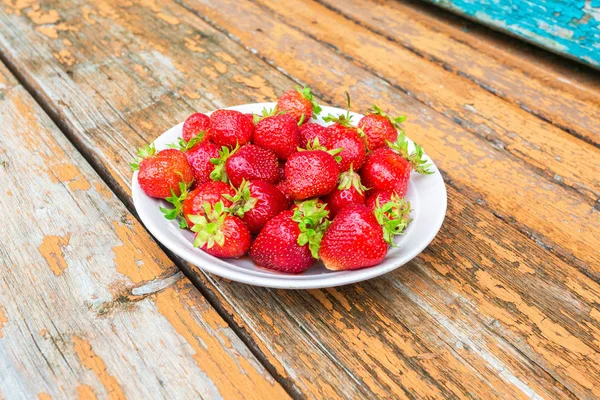 Fresh red strawberries in a white bowl standing on the rough woo — Stock Photo, Image