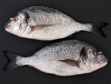 İki çiğ balık Dorado siyah bir taş zemin üzerine