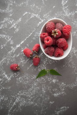 Bir masada gri taş beyaz bir kase içinde olgunlaşmış ahududu artığı