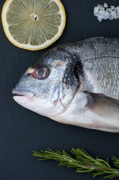 Peixe Dorado fresco, limão, alecrim e sal close-up em um preto — Fotografia de Stock