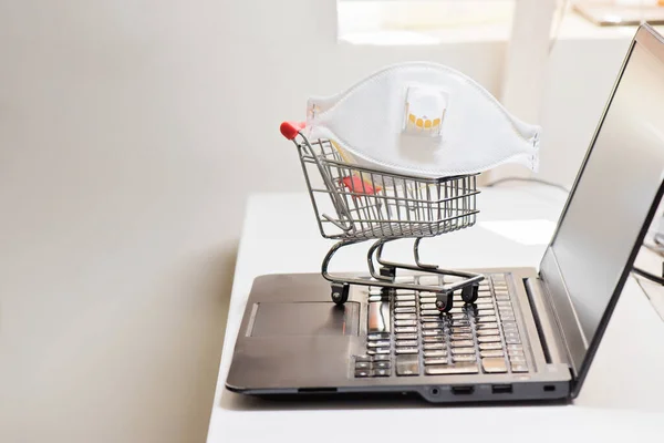 Conceptual photo with miniature shopping-cart and protecting mask. Safety internet shopping