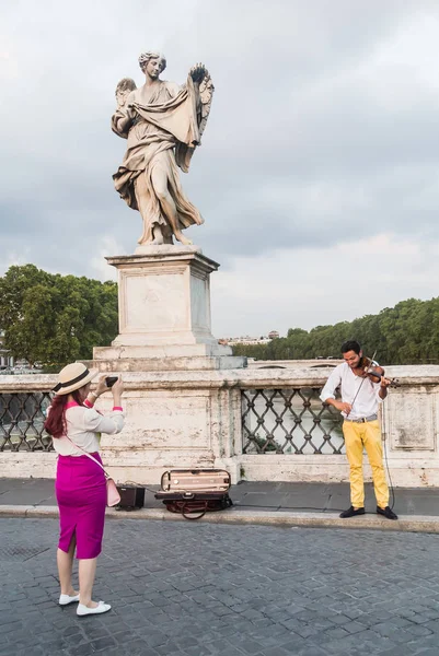 Egy turista fényképek a hegedűművész körül a szobrok-Szent Angelo hídon. Róma, Olaszország — Stock Fotó