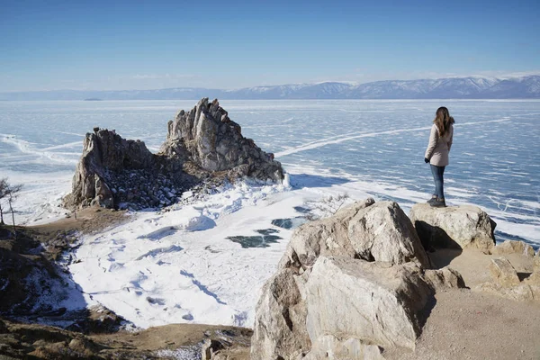 Lac Baïkal en hiver. Femme debout sur une falaise et regardant Burkhan Cape et Shaman Rock . — Photo