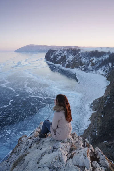 Lac Baïkal en hiver. Femme assise sur le bord d'une falaise et regardant le lac Baïkal gelé . — Photo