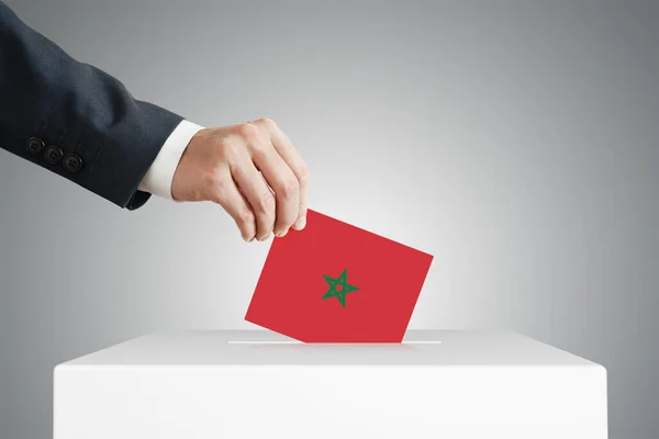 Man putting a voting ballot into a box with Morocco flag.