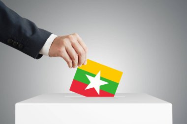 Myanmar bayrağıyla bir sandığa oy veren bir adam..