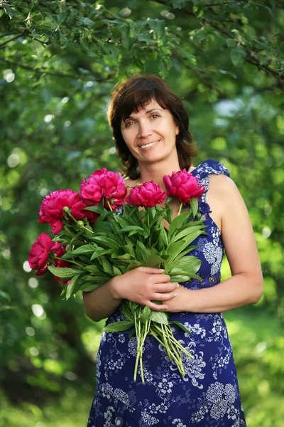 De vrouw van gemiddelde jaar met bloemen in een tuin — Stockfoto