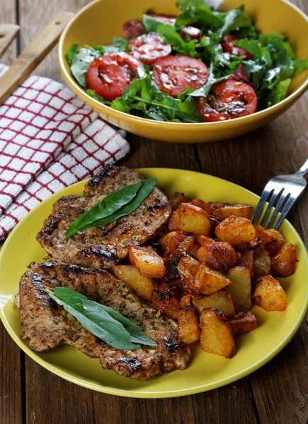 Patate fritte con carne e un piatto di insalata sul tavolo — Foto Stock