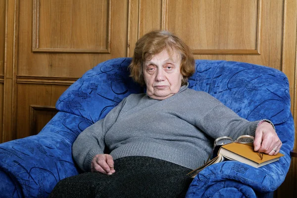 De oude vrouw in een fauteuil zit en leest het boek — Stockfoto